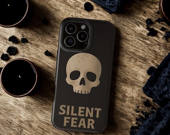 Puede incluir: Funda de teléfono negra con un diseño de calavera beige y la frase "SILENT FEAR" en el mismo color. La funda está sobre una superficie de madera, con dos velas negras y detalles de tela oscura.