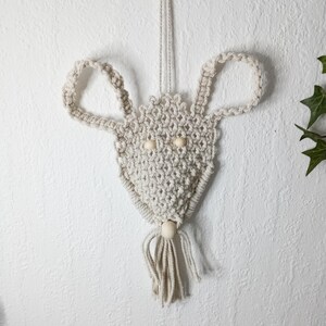 Könnte beinhalten: Ein weißer Makramee-Maus-Wandbehang mit Holzperlenaugen und einem Quasten.