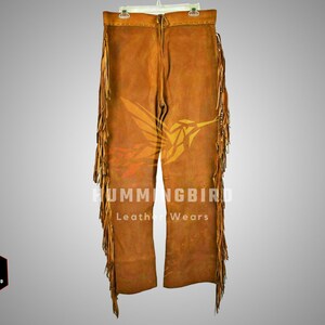 Puede incluir: Pantal&oacute;n de cuero marr&oacute;n con detalles de flecos y un dise&ntilde;o de colibr&iacute;. El pantal&oacute;n tiene una cremallera y trabillas para el cintur&oacute;n. "Hummingbird Leather Wears" est&aacute; impreso en el pantal&oacute;n.