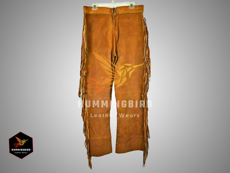 Puede incluir: Pantal&oacute;n de cuero marr&oacute;n con detalles de flecos y un dise&ntilde;o de colibr&iacute;. El pantal&oacute;n tiene una cremallera y trabillas para el cintur&oacute;n. "Hummingbird Leather Wears" est&aacute; impreso en el pantal&oacute;n.