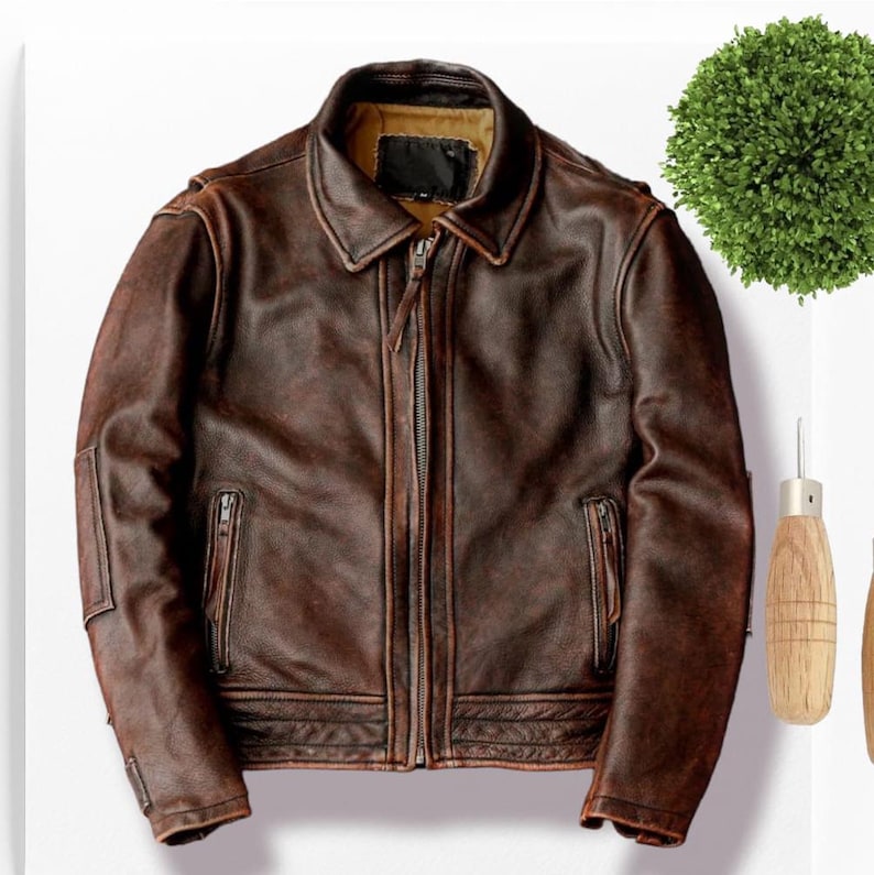 May include: A brown leather jacket with a zipper closure and a collared neckline. The jacket has a distressed look and features two zippered pockets on the front.
