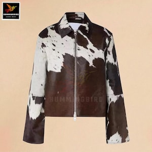 May include: A brown and white cowhide jacket with a zip closure and a collar. The jacket has long sleeves. The brand name "Hummingbird Leather Wears" is visible.