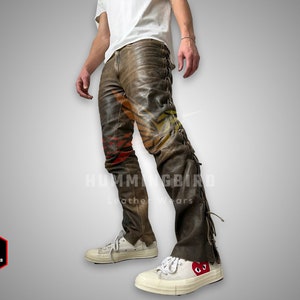 Puede incluir: Pantalón de cuero marrón con un estampado colorido y detalles de flecos. El pantalón se lleva con zapatillas blancas con un logotipo de corazón rojo.