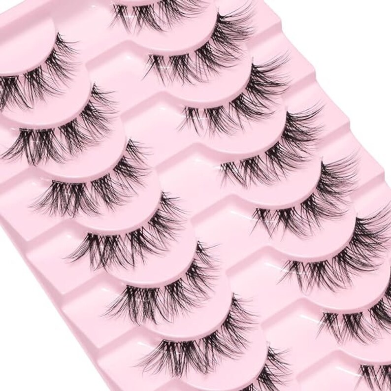 K&ouml;nnte beinhalten: Ein Set mit acht Paaren k&uuml;nstlicher Wimpern auf einer rosa Karte. Die Wimpern sind in Reihen angeordnet, wobei die l&auml;ngsten Wimpern oben und die k&uuml;rzesten unten sind.