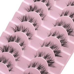 K&ouml;nnte beinhalten: Ein Set mit zehn einzelnen falschen Wimpern auf einer rosa Plastikpalette. Die Wimpern sind in Reihen angeordnet, wobei jede Reihe einen anderen Wimpernstil enth&auml;lt.