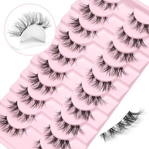 K&ouml;nnte beinhalten: Ein Set mit 10 Paaren k&uuml;nstlicher Wimpern auf einer rosa Karte. Die Wimpern sind in Reihen angeordnet, wobei jede Reihe einen anderen Wimpernstil enth&auml;lt. Die Wimpern sind alle schwarz und haben ein nat&uuml;rliches Aussehen.