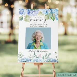 May include: A memorial sign on a wooden easel features a photo of a woman, surrounded by blue hydrangea illustrations and the text "In Loving Memory." The sign includes the name Amanda Hamilton and dates, with the phrase "always & forever."