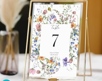 May include: A white table number card with a floral border. The card has the text "Table 7" and "Kate & Mark 08.09.2027".