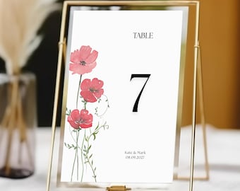May include: A white table number card with a red poppy floral design. The card reads "Table 7" and "Kate & Mark 08.09.2027".
