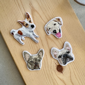 Peut inclure: Quatre écussons brodés de chiens. L'un représente un Jack Russell Terrier blanc, marron et noir. Un autre montre un Golden Retriever avec la langue sortie. Les deux autres écussons sont des bouledogues français.