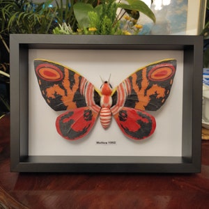 May include: A framed print of a red, black and white moth with the text "Mothra 1992" underneath.