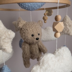 May include: A baby mobile with a brown teddy bear, white clouds, and blue stars hanging from a wooden ring.