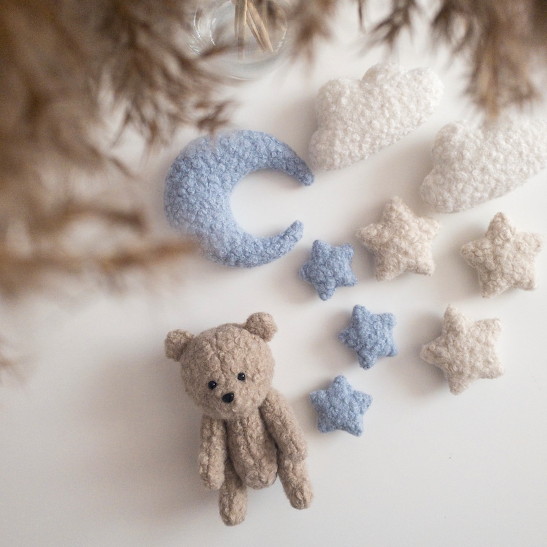 May include: A plush brown teddy bear with a blue crescent moon, white clouds, and blue and white stars. The plush toys are arranged on a white surface.