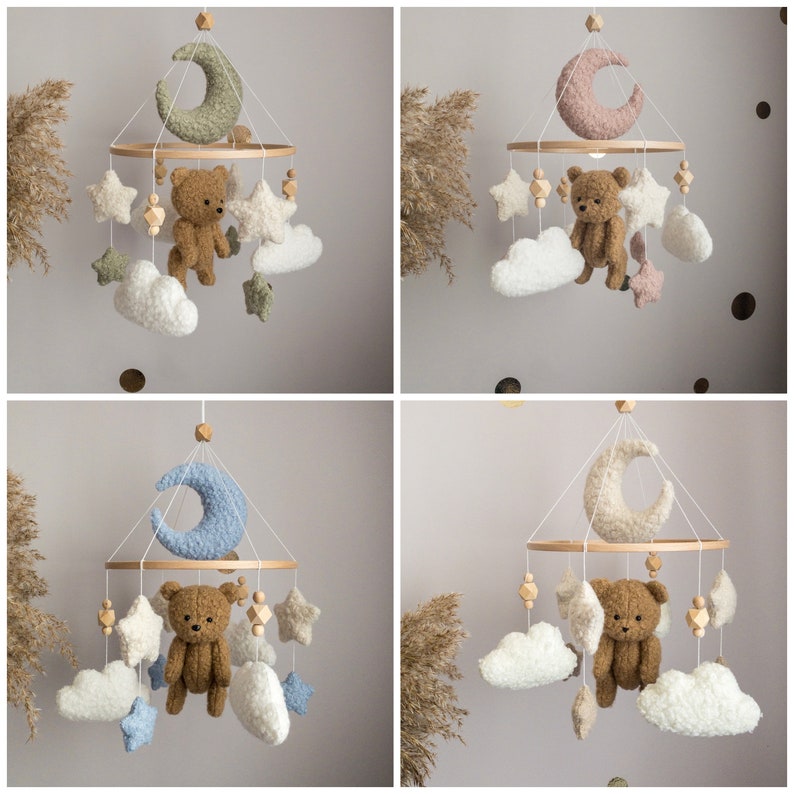 May include: A wooden baby mobile with a neutral color scheme. It features a crescent moon, stars, and clouds, all made of soft, fluffy fabric. A brown teddy bear hangs from the center of the mobile.