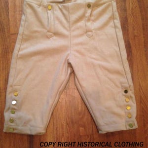 Może przedstawiać: Historyczne bryczesy w kolorze beżowym ze złotymi guzikami po bokach i z przodu. Bryczesy mają wysoki stan i są wykonane z miękkiej tkaniny. Tekst "COPY RIGHT HISTORICAL CLOTHING" jest widoczny na dole.