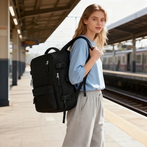 May include: A black backpack with a quilted pattern, multiple compartments, and adjustable straps. The backpack has a top handle and side buckles. The image shows the backpack on a person at a train station.
