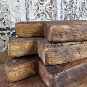 May include: Close-up of four stacked, rustic wooden shelves. The shelves are made of thick, weathered wood with visible grain and knots. The wood has a warm, natural color with variations in tone, suggesting a handmade or reclaimed aesthetic.