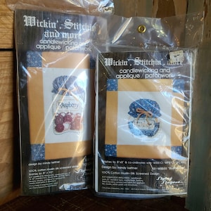 May include: Two embroidery kits for candlewicking and applique. The kits are packaged in plastic bags and feature images of jars labeled "Raspberry" and "Blueberry". Each kit includes 100% cotton muslin silk screened designs and finishes to 8 inches by 8 inches or 8 inches by 10 inches.