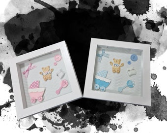 Puede incluir: Dos marcos de fotos blancos con un tema de bebé azul y rosa. Los marcos contienen un osito de peluche, un cochecito, un sonajero y otros artículos para bebés. Los marcos están sobre un fondo blanco con salpicaduras de acuarela negra.