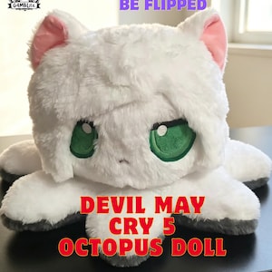 Könnte beinhalten: Eine weiße Plüsch-Oktopus-Puppe mit grünen Augen und rosa Innenohren. Die Puppe trägt den Text "25CM DOLL, CAN BE FLIPPED" und "DEVIL MAY CRY 5 OCTOPUS DOLL" im Bild. Die Puppe ist etwa 25 cm groß.