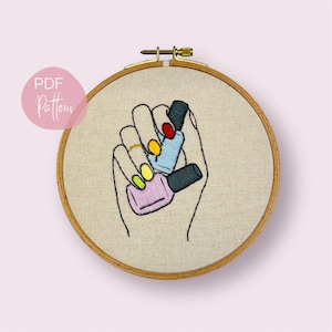 May include: Embroidered design of a hand holding four nail polish bottles. The bottles are in shades of pink, blue, green, and red. The nails on the hand are painted in various colors.