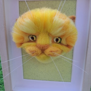 Framed yellow needle felted cat face.