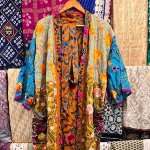 Könnte beinhalten: Ein langer, mehrfarbiger Kimono mit floralem Muster und einem Ärmel mit blau-weißem Muster. Der Kimono ist aus einem leichten Stoff gefertigt und hat einen Bindeverschluss an der Vorderseite.