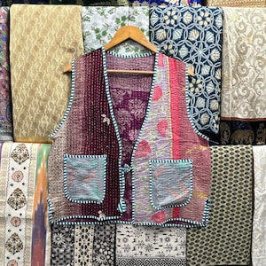Könnte beinhalten: Eine gesteppte Weste aus Patchwork in Lila, Rosa und Blau mit einem Bindeverschluss. Die Weste hat zwei Taschen und ist aus recycelten Saris gefertigt.