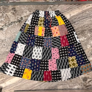 May include: A black skirt with a patchwork design featuring various colourful patterns, including geometric shapes, eyeglasses, and animals. The skirt has a drawstring waist.
