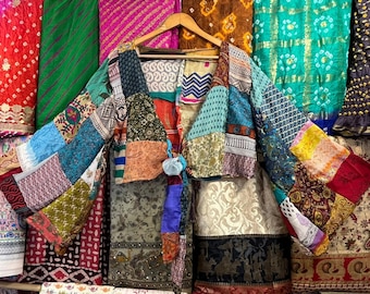 May include: A colourful patchwork jacket made from upcycled fabric. The jacket has a cropped silhouette and a tie closure at the front. The fabric is a mix of different patterns and colours, including blue, green, red, and yellow.