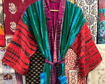 May include: A colorful tie-dye robe with a green, blue, and purple pattern. The robe has a long sleeve and a sash tie. The robe is displayed against a background of colorful fabrics.