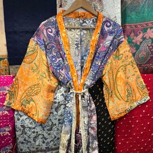 Puede incluir: Un kimono de seda colorido con estampado paisley y detalles en naranja, azul y morado. El kimono se ata a la cintura con una cinta y tiene mangas largas.