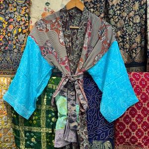 May include: A patchwork kimono robe in a blue, green and brown colour scheme. The robe has a tie belt and long sleeves. The fabric is a mix of silk and cotton.