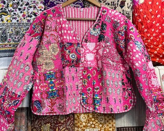 Puede incluir: Una chaqueta acolchada rosa con un diseño de patchwork. La chaqueta tiene cuello en V y cierre de botón. La tela es una mezcla de patrones florales y geométricos.