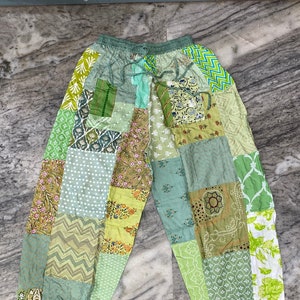 May include: Green patchwork pants with a drawstring waist. The pants are made of different fabrics with various patterns, including floral, geometric, and paisley.