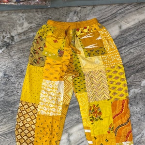 May include: Yellow patchwork pants with a drawstring waist. The pants are made of different fabrics with various patterns, including floral, geometric, and paisley.