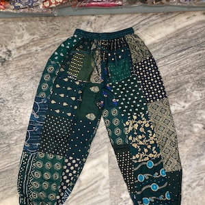 Può includere: Pantaloni verdi in patchwork con vita a coulisse e una varietà di motivi in oro e blu.