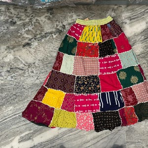 Könnte beinhalten: Ein Patchwork-Rock mit einer Vielzahl farbenfroher Stoffquadrate. Der Rock hat einen gelben Kordelzugbund und eine ausgestellte Silhouette. Die Quadrate sind in Rosa-, Gelb-, Grün-, Rot- und Blautönen mit verschiedenen Mustern und Texturen.