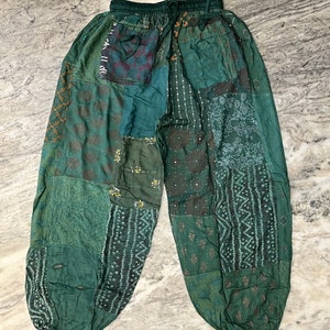 Pode incluir: Calças verdes de patchwork com cós elástico e cordão. As calças apresentam várias tonalidades de tecido verde com padrões bordados e estampados. As calças folgadas têm uma bainha franzida e um estilo descontraído.