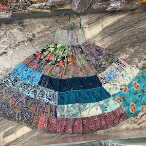 Może przedstawiać: Sukienka w stylu patchwork z różnymi kolorowymi wzorami kwiatowymi i paisley. Sukienka ma dopasowany gorset i rozkloszowaną spódnicę.