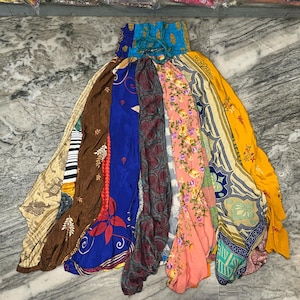 May include: A colorful, patchwork skirt made from various patterned fabrics. The skirt features a gathered waistband and a flowing, layered design. The fabrics include floral prints, geometric patterns, and solid colors like blue, brown, and yellow.