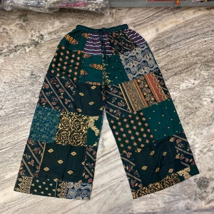 Pode incluir: Calças verdes de patchwork com uma variedade de padrões coloridos e detalhes dourados.