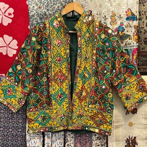 Può includere: Una giacca ricamata gialla, verde e rossa con decorazioni a specchio. La giacca ha un colletto alla coreana e una chiusura frontale.