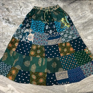 Könnte beinhalten: Ein langer Patchwork-Rock in Grün- und Blautönen. Der Rock besteht aus verschiedenen Stoffen mit unterschiedlichen Mustern, darunter Blumen-, geometrische und Paisley-Muster.