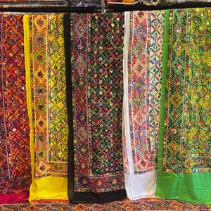 Peut inclure: Six panneaux de tissu brodés colorés avec des motifs complexes et des embellissements en miroir. Les panneaux sont suspendus à un rack et sont tous de couleurs et de motifs différents.