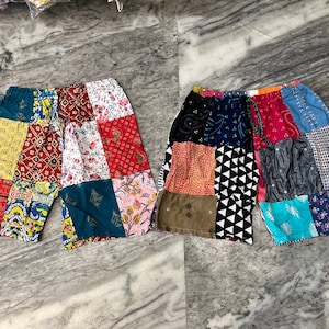 Może przedstawiać: Dwie pary krótkich spodenek patchwork z różnymi kolorowymi wzorami, w tym kwiatowymi, geometrycznymi i paisley.