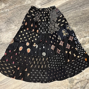 Pode incluir: Uma saia preta em camadas com um design de patchwork que apresenta vários padrões em dourado, branco e rosa. A saia tem uma cintura elástica e uma silhueta fluida.