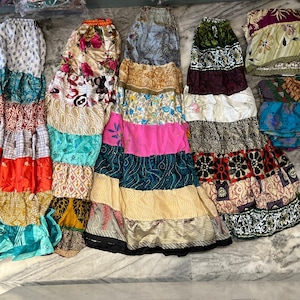 Può includere: Una collezione di gonne a strati colorate realizzate con tessuto patchwork. Le gonne presentano una varietà di motivi e colori, tra cui disegni floreali, geometrici e astratti. Le gonne sono disposte su una superficie chiara.