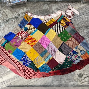 May include: A colorful patchwork wrap skirt made from various fabrics in shades of pink, blue, green, yellow, and red. The skirt is tied at the waist with a long sash.