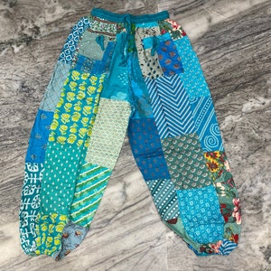 Puede incluir: Pantalones de patchwork con un esquema de color azul y verde. Los pantalones tienen una cintura con cordón y un ajuste holgado.